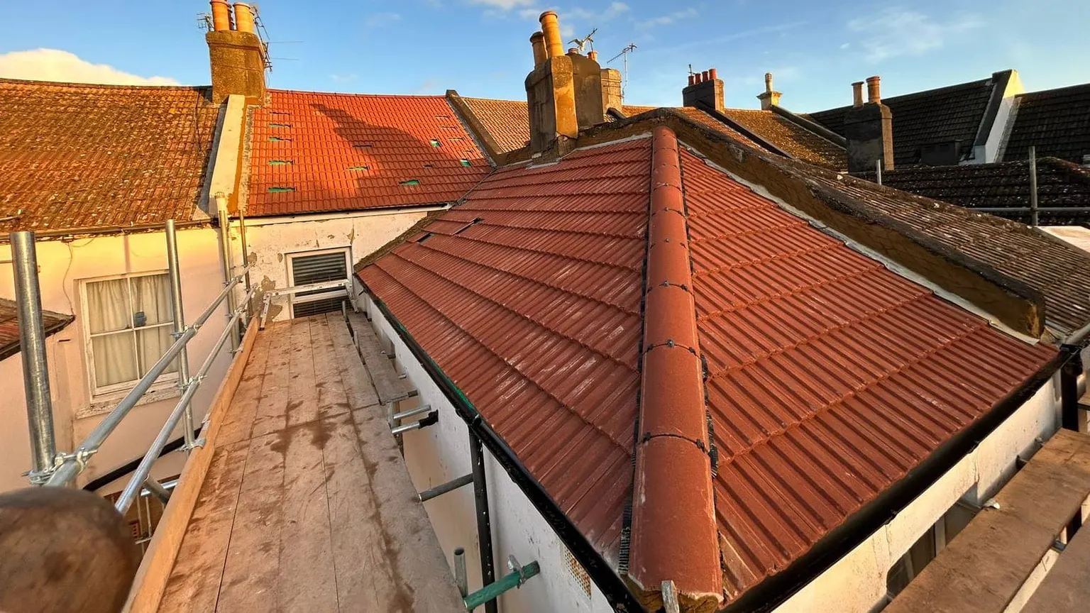A completed re-roof in new red tiles by Masters Roofing, with chimneys and neighbouring rooftops beyond