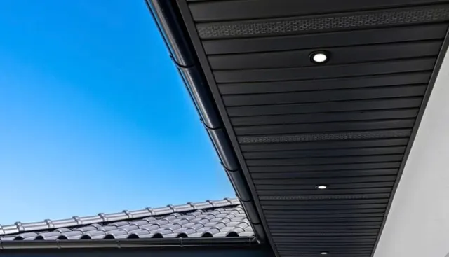 A black vented soffit with recessed downlights fitted under a tiled roof edge