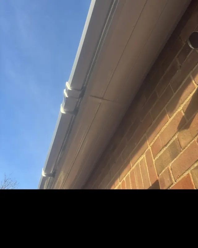 A new white fascia, soffit and gutter run along the eaves of a brick house