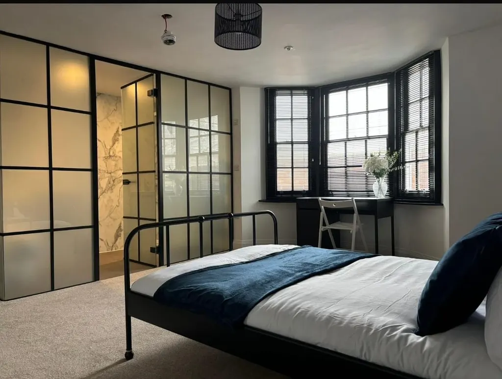 A finished bedroom in a converted property, with a glazed steel-framed partition to the en-suite