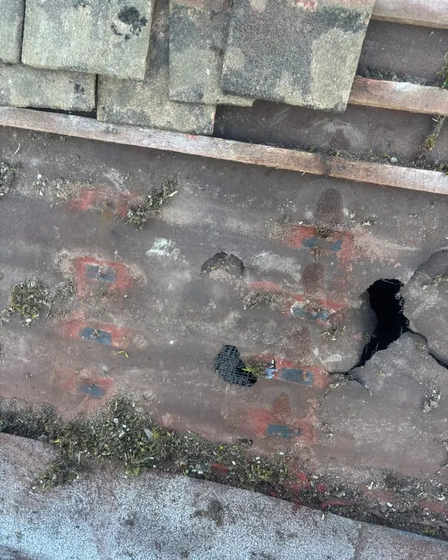 Cracked and holed roof tiles on a weathered pitched roof, photographed before repair