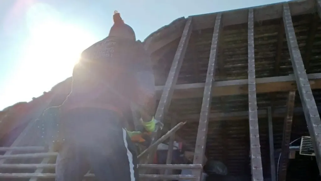 A Masters Roofing roofer working on a stripped roof with the sun behind the rafters